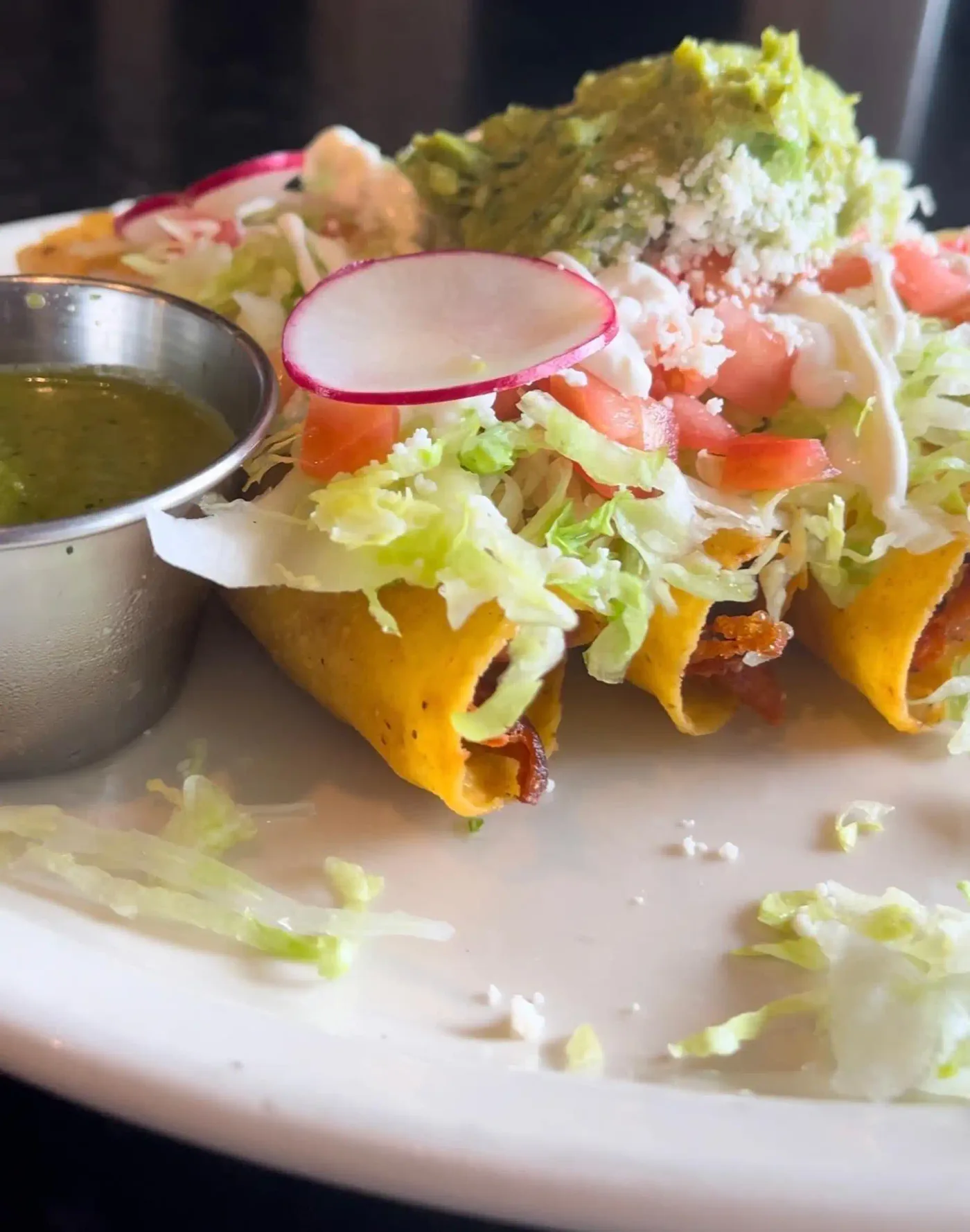 Crispy flautas topped with lettuce, tomato, crema, and queso fresco