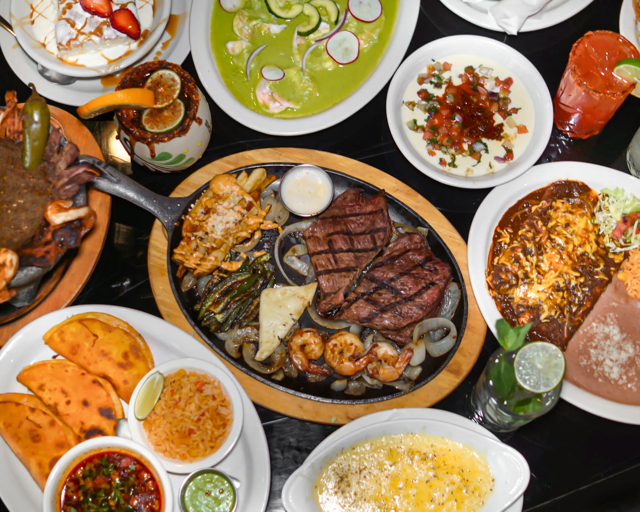 A full spread of Mas Amigos Mexican dishes with margaritas and micheladas